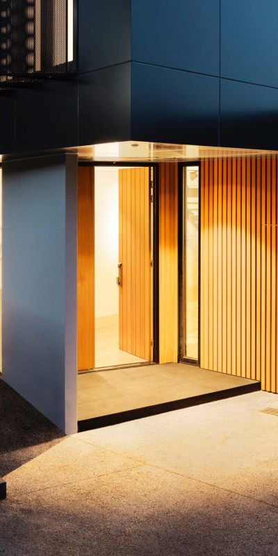 Modern house exterior with wooden and concrete elements, illuminated by warm lighting.